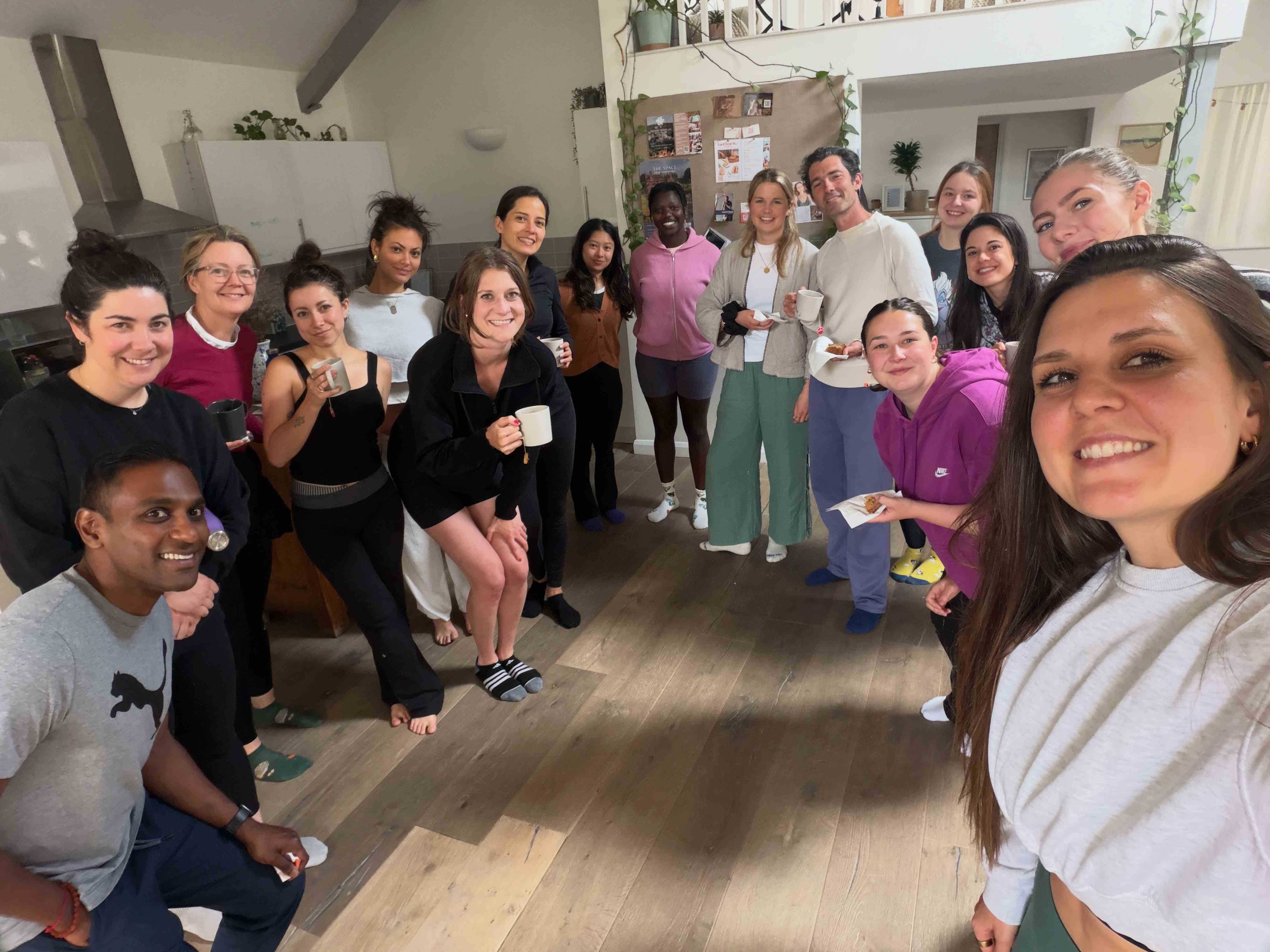 A large smiling group of people gathered in a warm studio space after a community wellbeing session